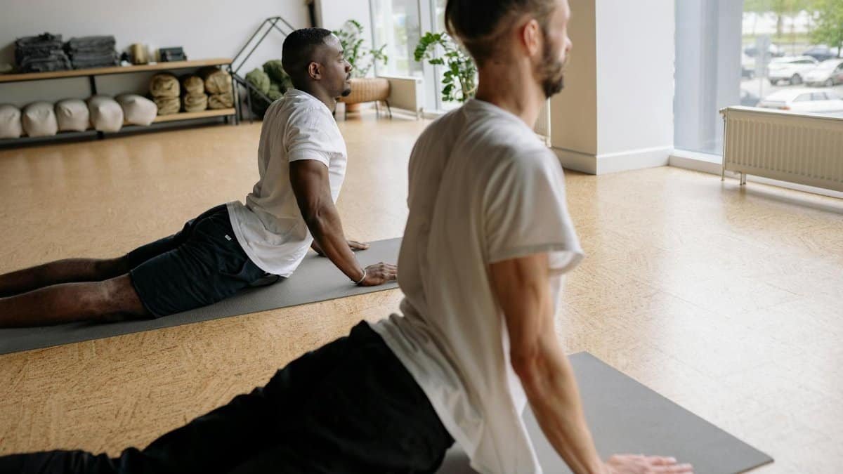 Two men stretching in yoga poses on mats in a serene indoor studio setting.