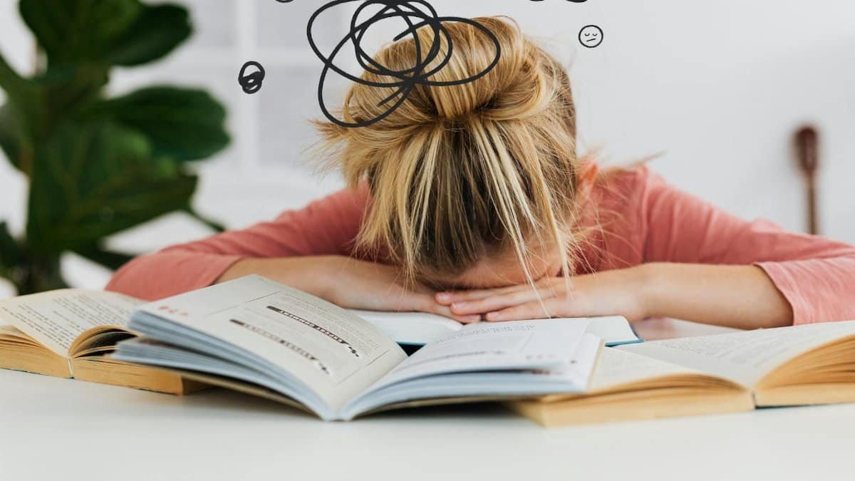 Young woman asleep over books at desk, conveying stress and mental overload.