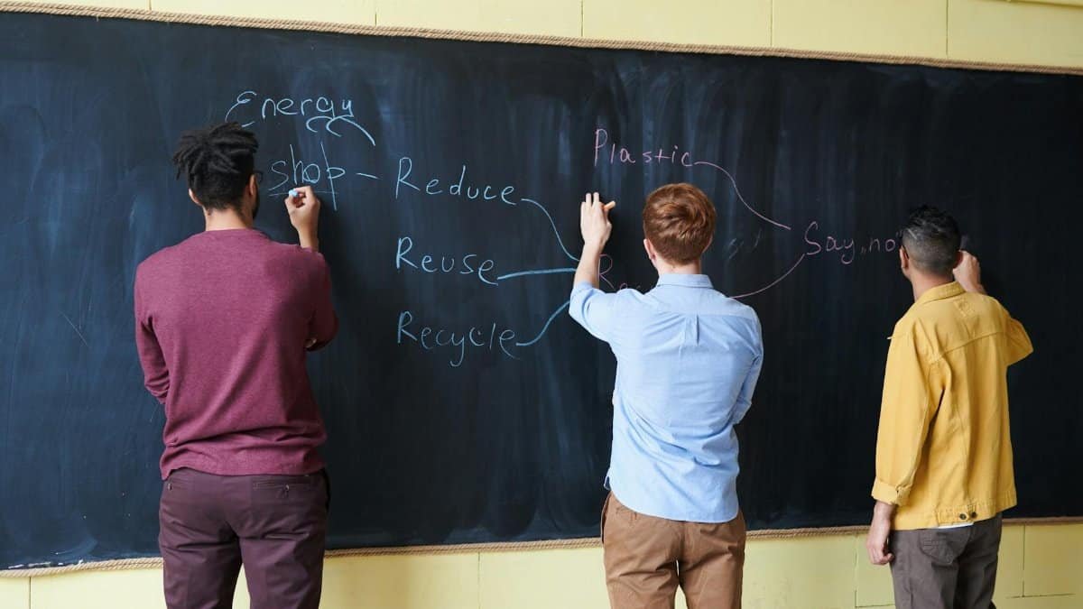 Three students writing on a chalkboard, focusing on reducing plastic and energy waste.