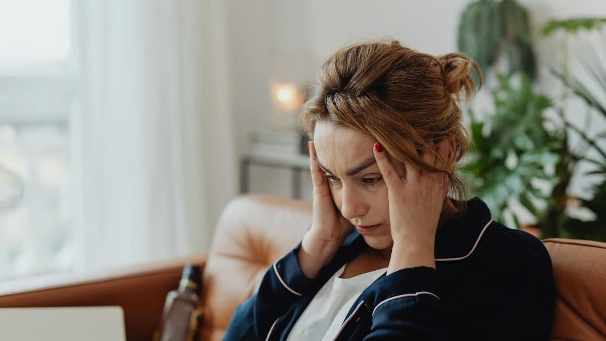 A woman in pajamas sits indoors with hands on head, showing stress and frustration. Perfect for mental health themes.