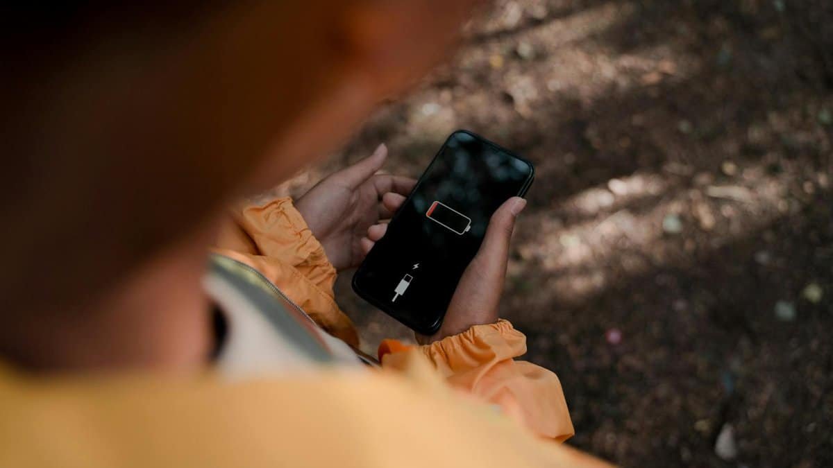 Teenage boy holds a smartphone displaying low battery outdoors in a forest.