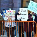 A group of people holding signs in a street protest, expressing dissent against political policies.
