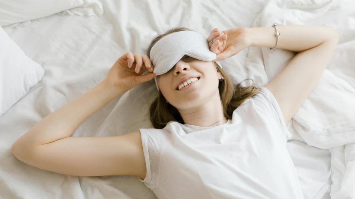 A serene young woman enjoying relaxation with a sleep mask in her cozy bed.