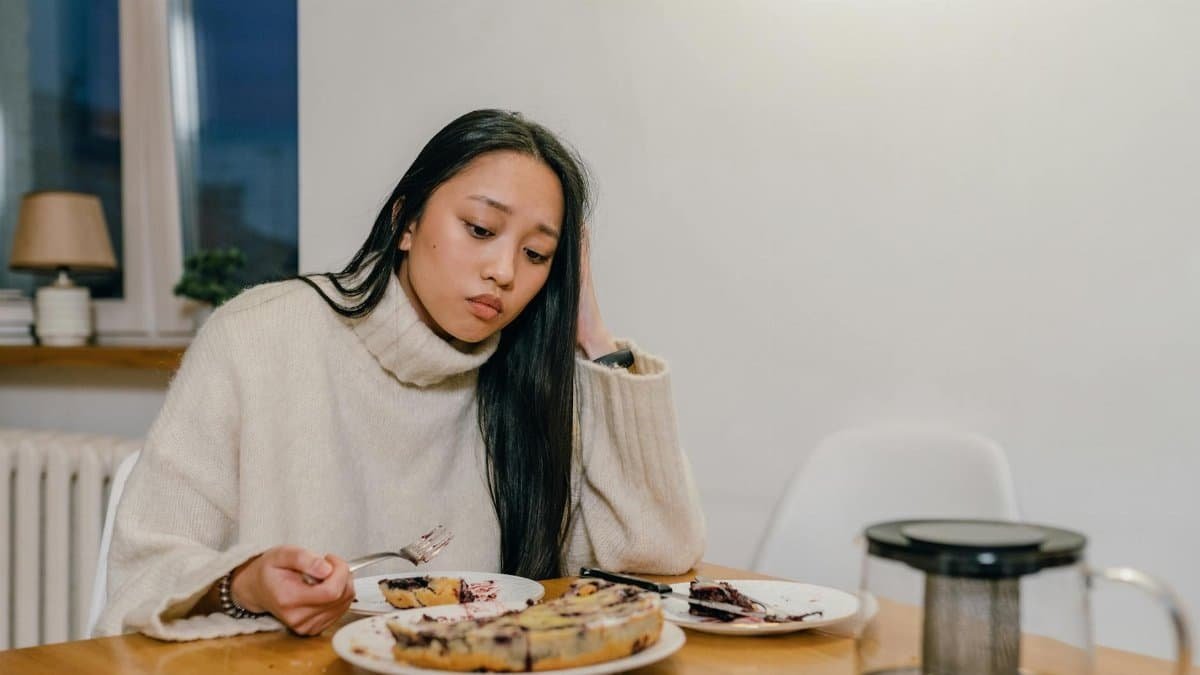 A thoughtful woman in a cozy sweater eats dessert alone, reflecting deep thoughts.