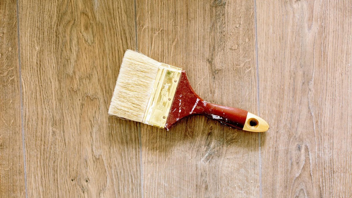 A used paintbrush lying on a wooden floor, ideal for renovation and DIY themes.