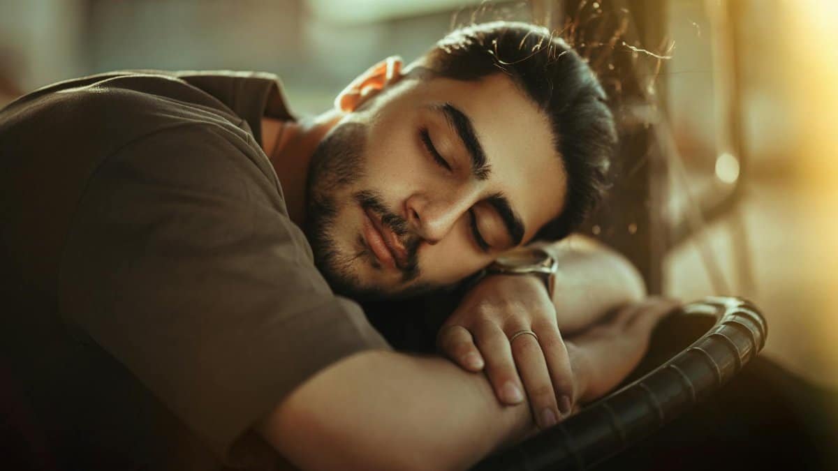 Young man sleeping with closed eyes, resting peacefully in warm sunlight, creating a tranquil scene.