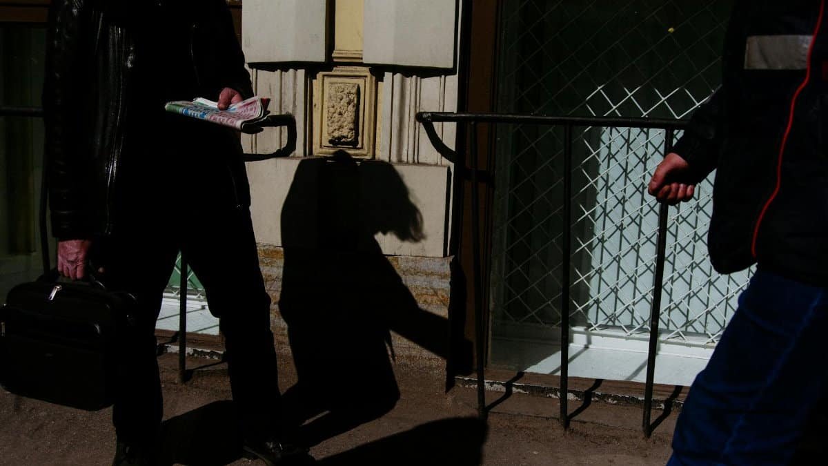 Man reading newspaper in urban setting casting intriguing shadows.