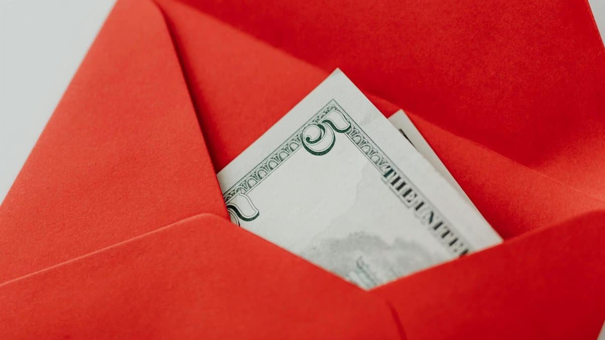 A close-up of a US dollar bill partially visible in a bright red envelope, symbolizing gifting or financial reward.