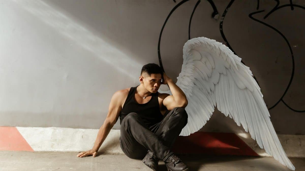 A thoughtful man with angelic white wings, sitting in a modern urban environment, deep in reflection.