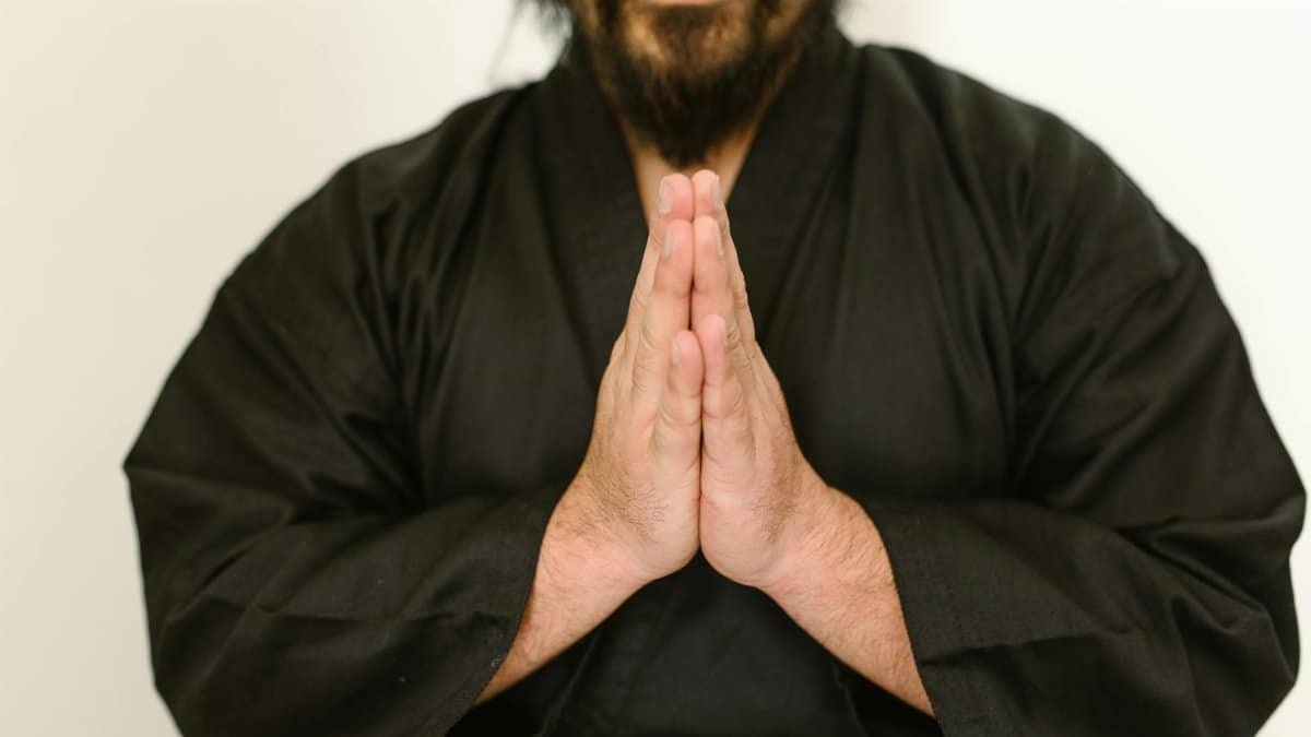 A focused martial artist in a black gi with hands in prayer position, indoors.