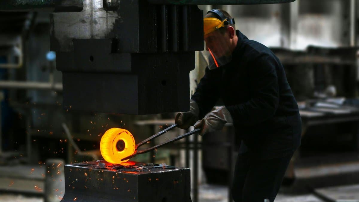 A blacksmith skillfully working with red-hot metal in an industrial setting, showcasing craftsmanship.