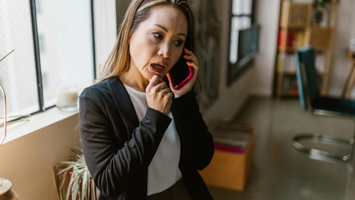 Professional Asian woman talking on her smartphone indoors, emphasizing work from home atmosphere.