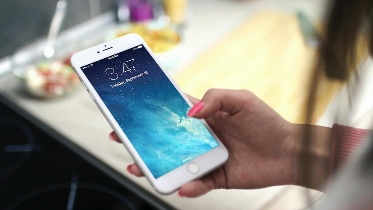 Close-up shot of a person holding a smartphone in a kitchen setting, displaying the lock screen.