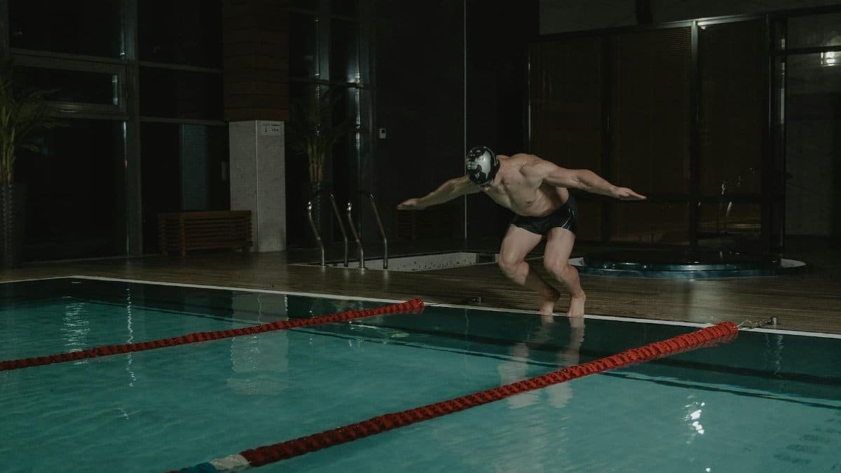 Athlete diving into an indoor swimming pool at night, showcasing fitness and energy.
