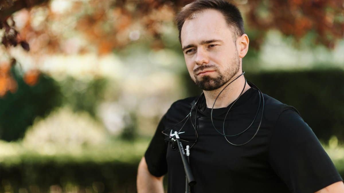 Bearded man in black shirt outdoors with a skipping rope around his neck, ready for exercise.
