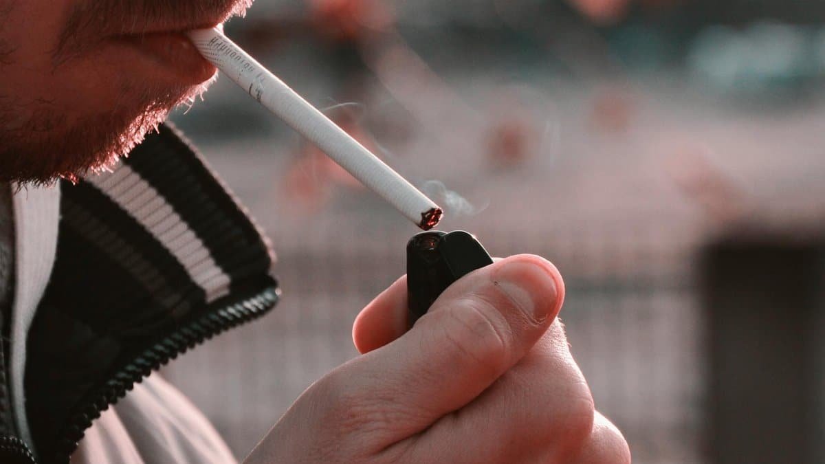 Close-up image of a person lighting a cigarette with a lighter outdoors, highlighting smoking habits.