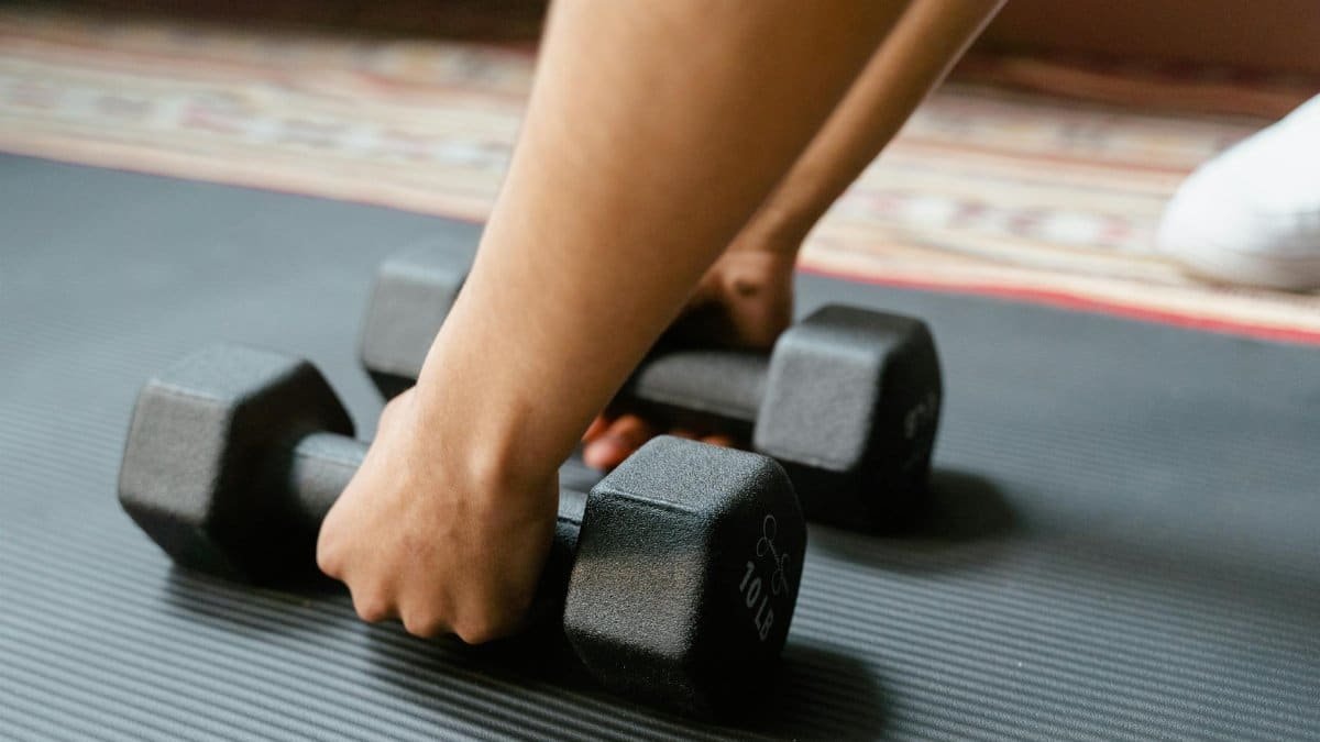 Close-up of a person picking up dumbbells on a yoga mat, emphasizing fitness and exercise.