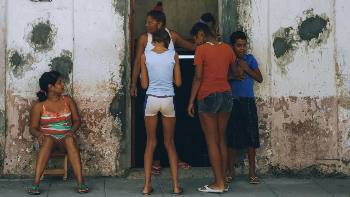 Family members stand on a sidewalk outside a weathered building, interacting warmly.