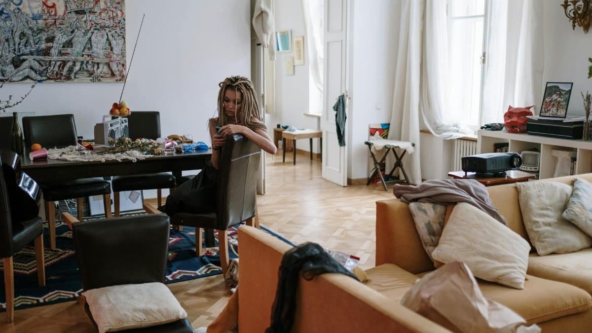 Woman with dreadlocks sitting in a cozy, cluttered room checking her smartphone.