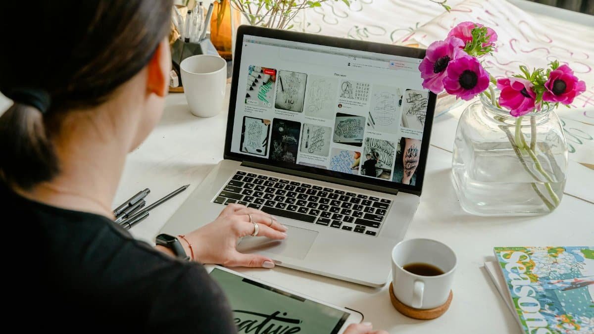Woman in a creative workspace using a laptop and tablet for calligraphy. Artistic and tech-driven environment.