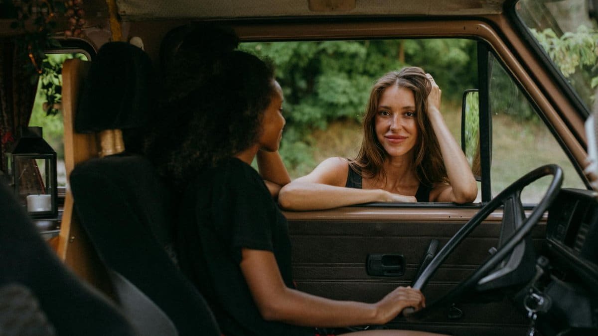 Two women on a road trip enjoying a moment inside a camper van amidst a lush landscape.