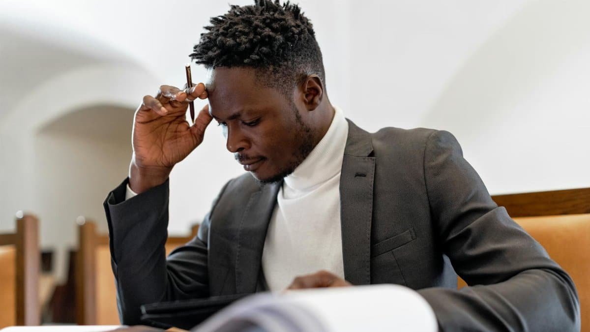 A focused businessman in a suit examines documents while deep in thought in an office setting.