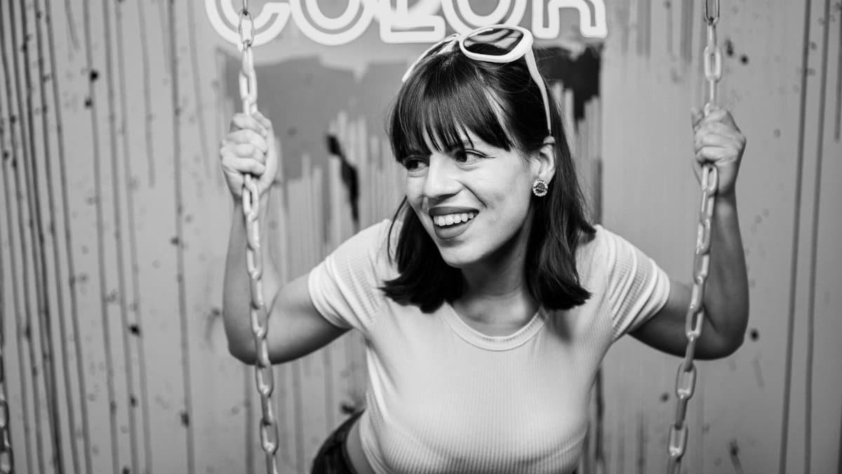 Black and white portrait of a smiling brunette woman holding onto a swing indoors.