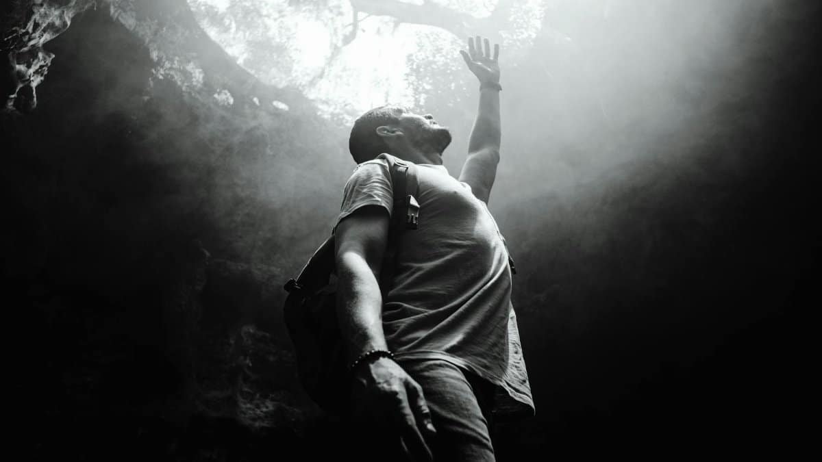 A man reaches towards sunlight inside a cave, evoking adventure and exploration.