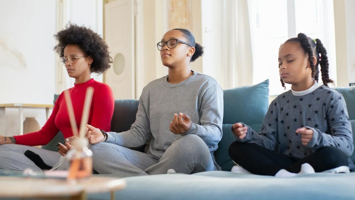 A family of three meditates together on a living room couch, promoting mindfulness.