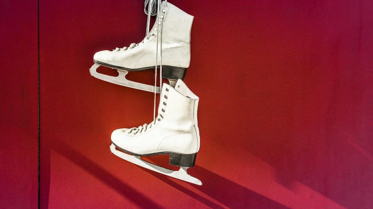 Pair of white ice skates hanging on a vibrant red wall, perfect for winter sports imagery.