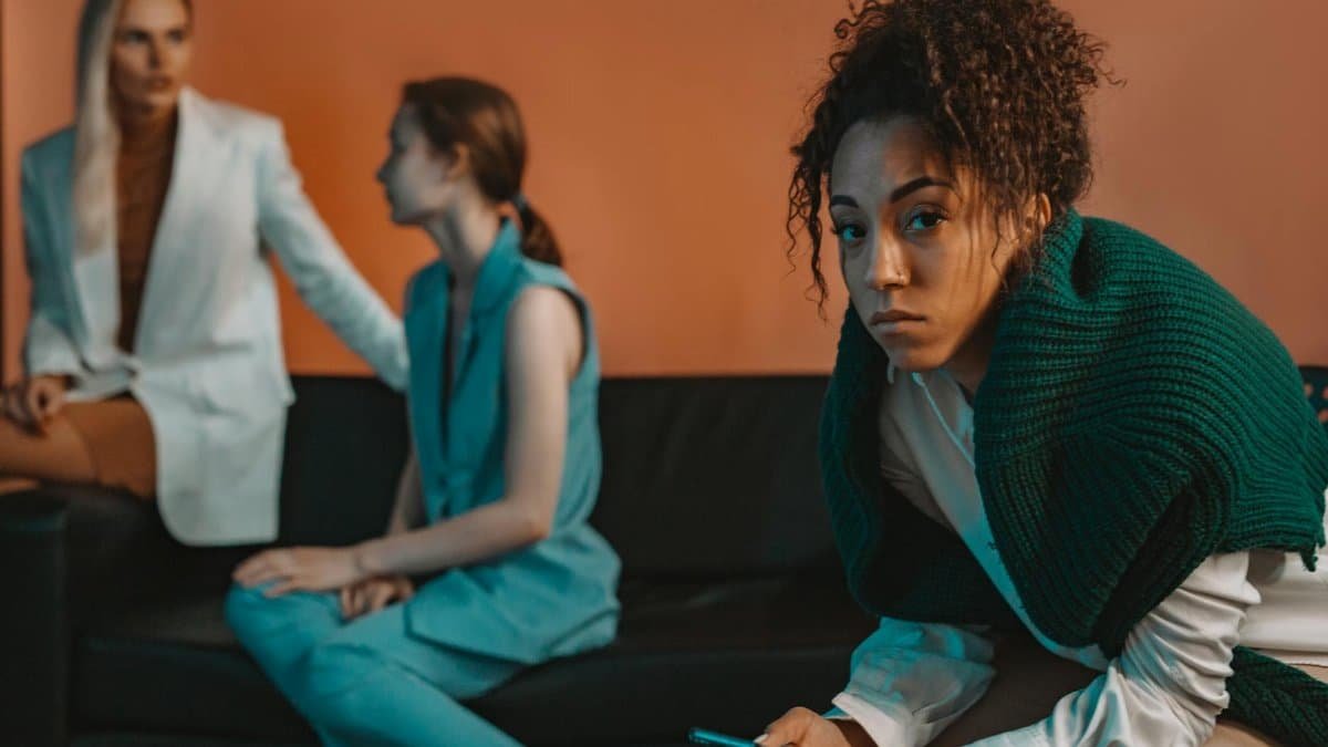 Three women sitting on a couch, displaying a range of emotions and social dynamics in an indoor setting.