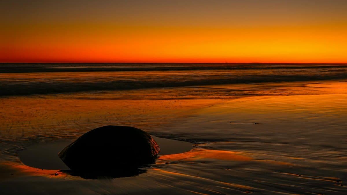 Captivating sunset over a tranquil beach with distinctive rock formation.