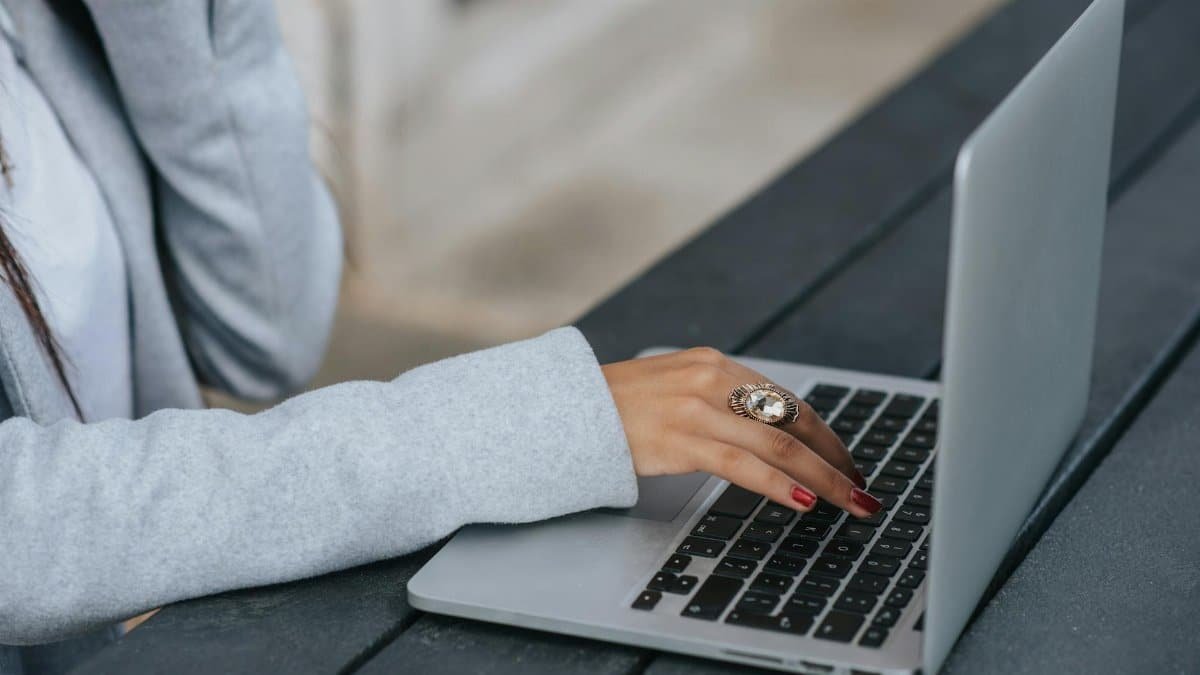 Side view of crop anonymous female entrepreneur in luxury ring working on netbook at wooden table