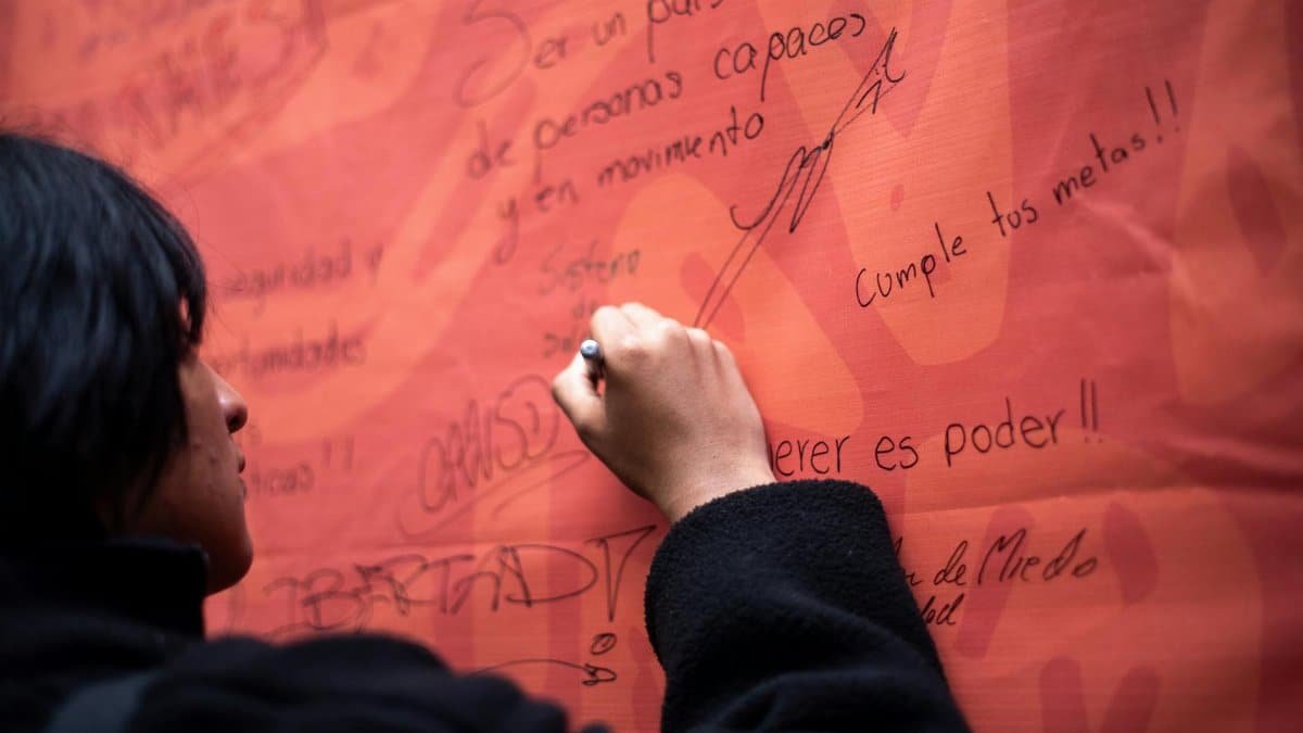 A person writing motivational messages on a large orange banner with handwritten text.