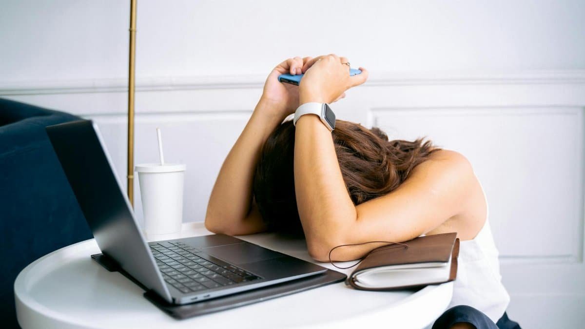 Young woman showing stress with laptop and phone at desk, embodying digital exhaustion.