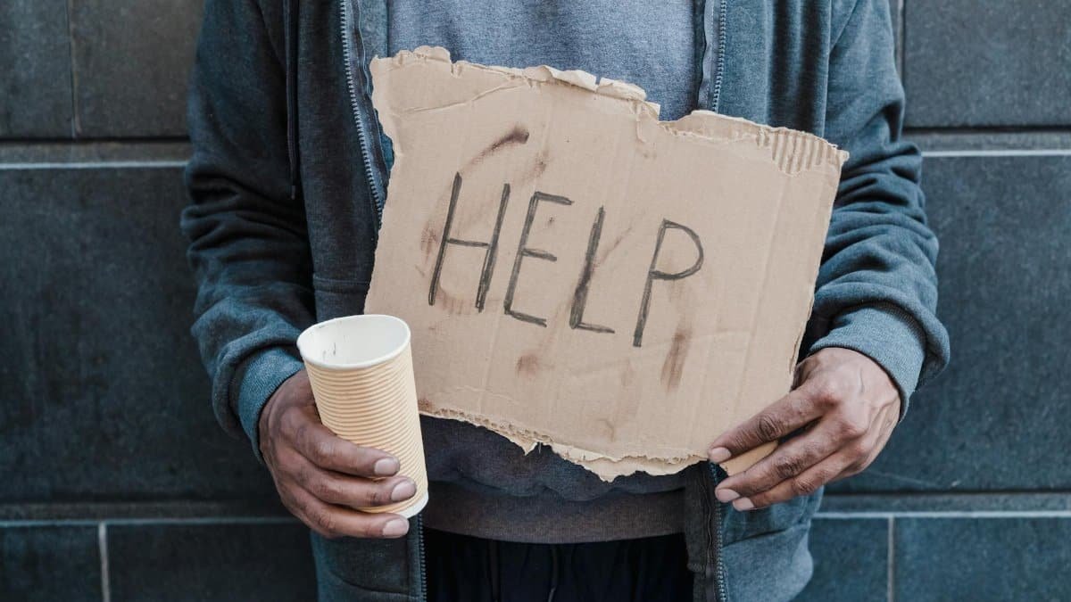 Close-up of a person holding a help sign and paper cup, highlighting social issues.