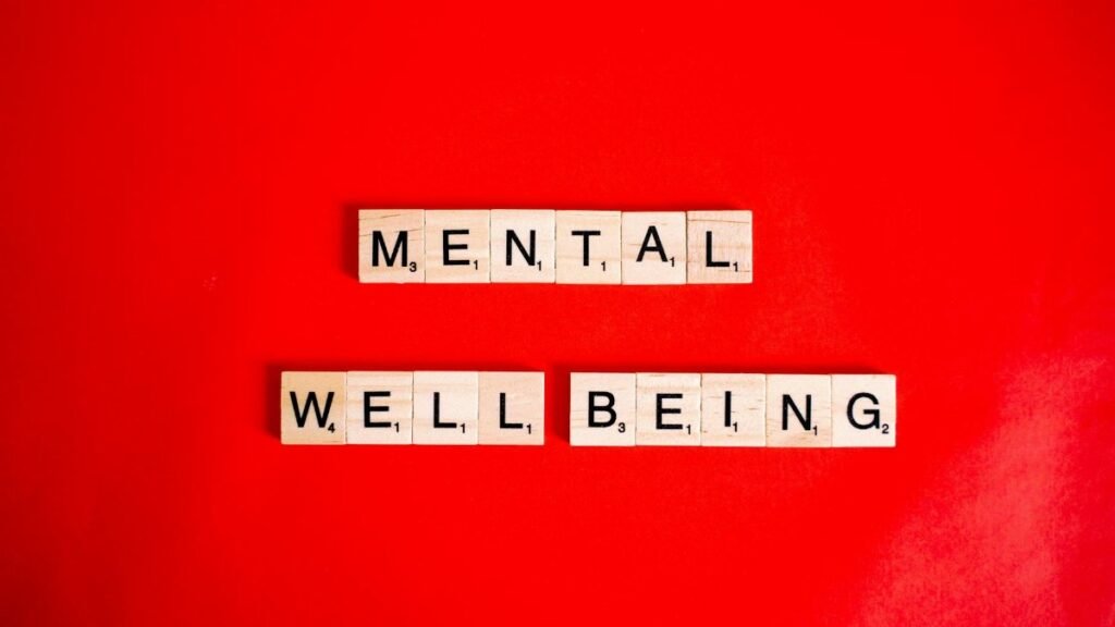Wooden Scrabble tiles spelling 'mental wellbeing' on a vibrant red background.