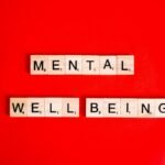 Wooden Scrabble tiles spelling 'mental wellbeing' on a vibrant red background.