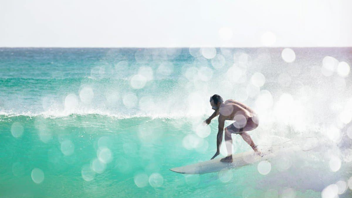 An adult surfer skillfully rides a wave in the clear waters of Queensland, Australia.