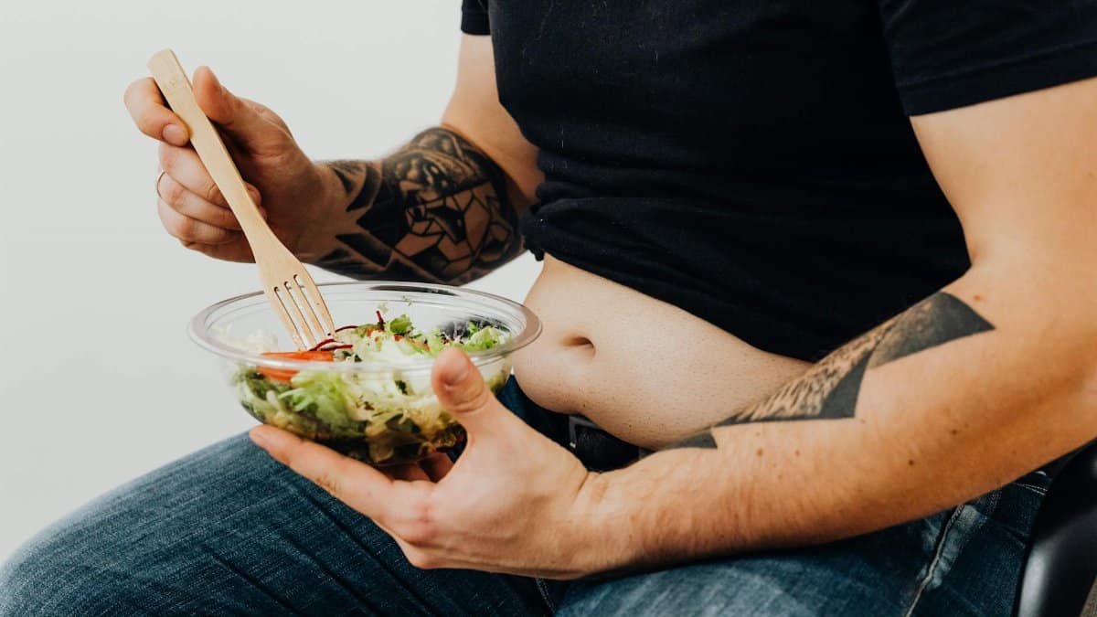 A tattooed individual holding a fresh salad, symbolizing healthy lifestyle and fitness motivation.