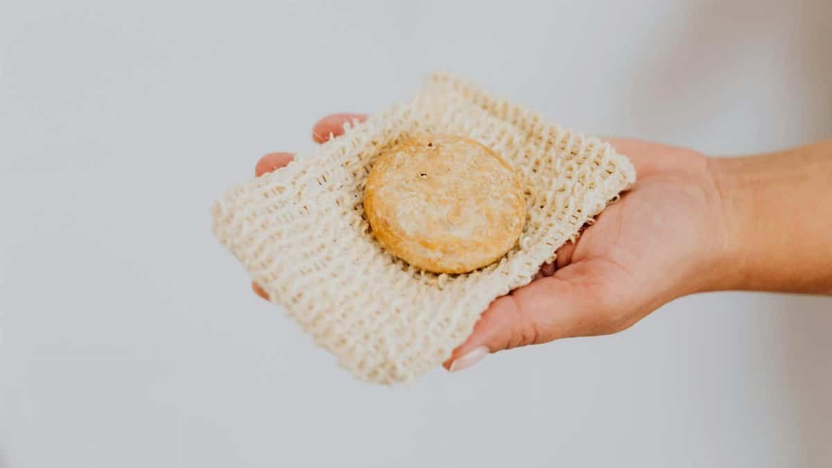 A hand holding eco-friendly handmade soap on a natural loofah pad, promoting sustainable skincare.
