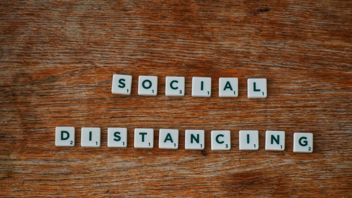 Scrabble tiles spelling out 'social distancing' on a wooden surface.