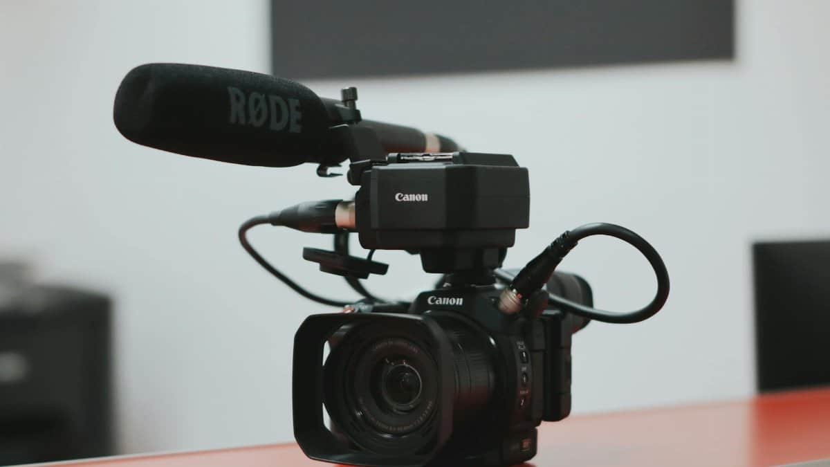 Close-up of a professional video camera setup with Rode microphone on a desk.