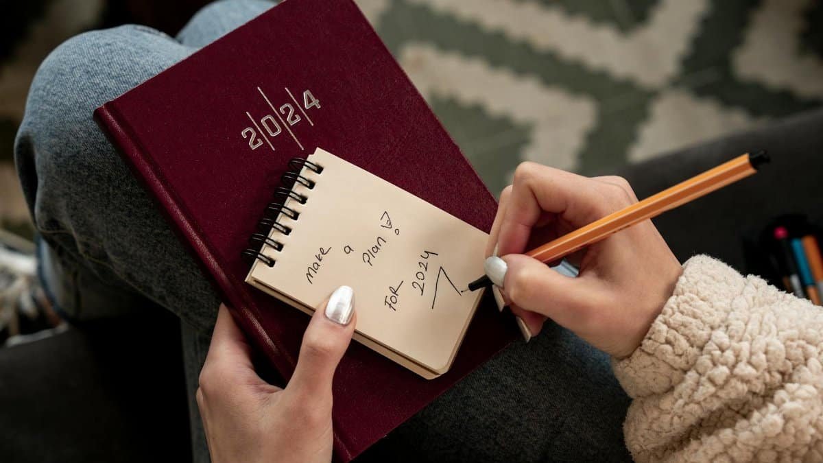 Woman writing future plans in a 2024 planner with focus on personal goals and organization.