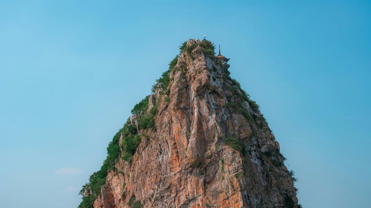 A majestic rocky cliff rises against a clear blue sky, creating a stunning outdoor landscape.