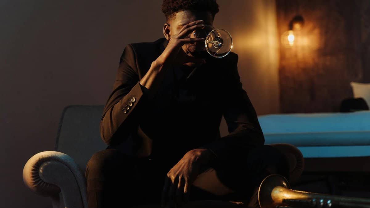 Elegantly dressed man in black suit savoring wine indoors, capturing a moment of luxury and relaxation.