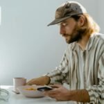 A man enjoys a casual breakfast with cereal in a sunlit room, using his phone.