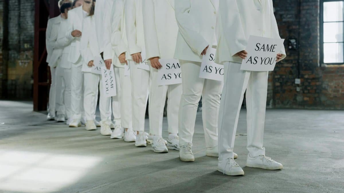 A group of individuals in white suits holding 'Same as You' signs, symbolizing unity and conformity.