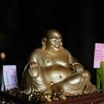 Gold Laughing Buddha statue adorned with donation signs and coins, symbolizing prosperity.