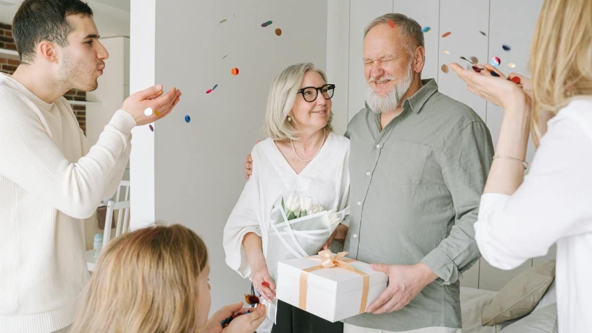 Happy elderly couple receives gifts and love from family during an indoor celebration.